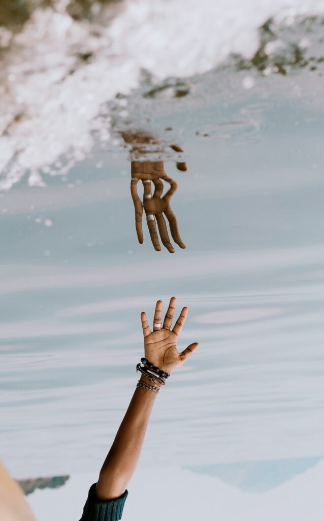 Photo d'une main tendue dans l'eau. Elle se reflète comme un miroir, à la verticale.