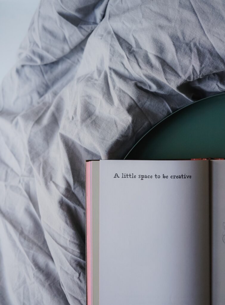 Photo d'un livre, ouvert sur la couette d'un lit. Il y est inscrit en anglais "petit espace pour être créatif".