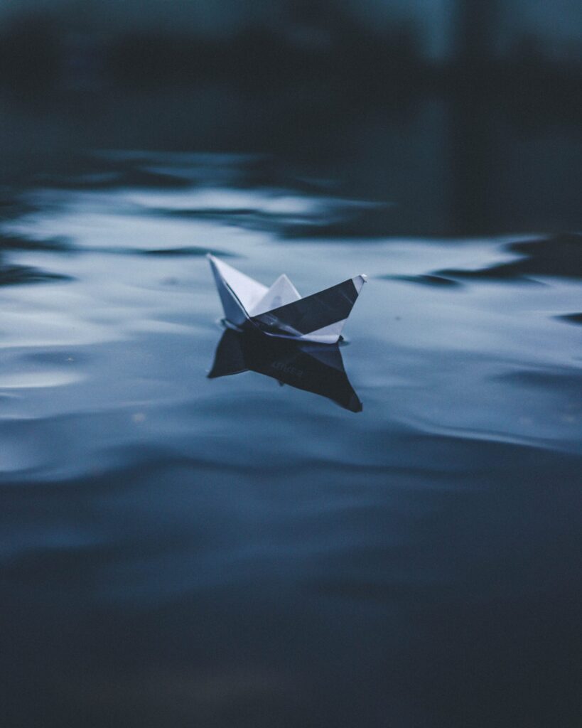 Photo d'un bateau en papier, posé sur l'eau. Tout semble calme et serein.