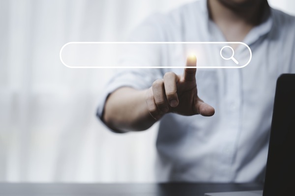 Image d'un homme qui appuie, face à nous, sur un écran transparent, sur la barre de résultats de recherche. Il cherche une réponse à ses questions et espère trouver un article de blog intéressant sur la SERP comme sur l'IA.